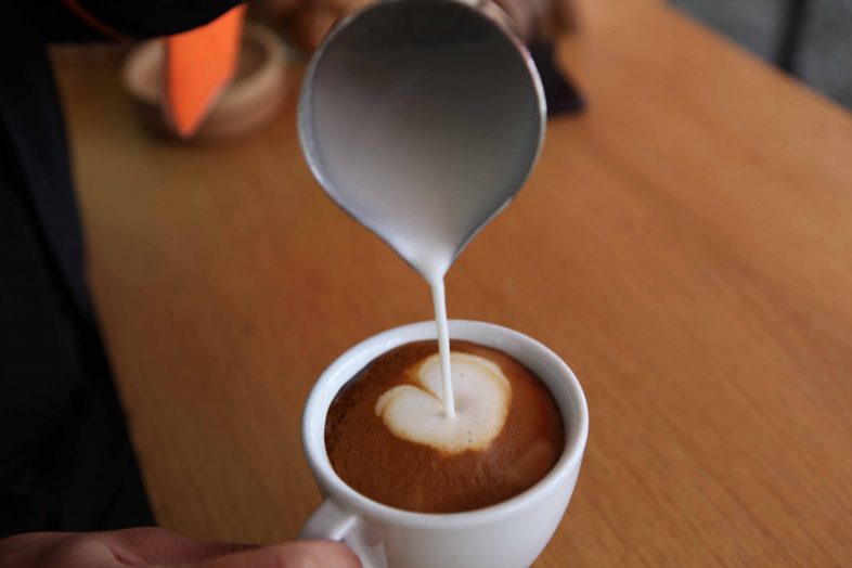 Milch wird in einen Kaffee geschüttet